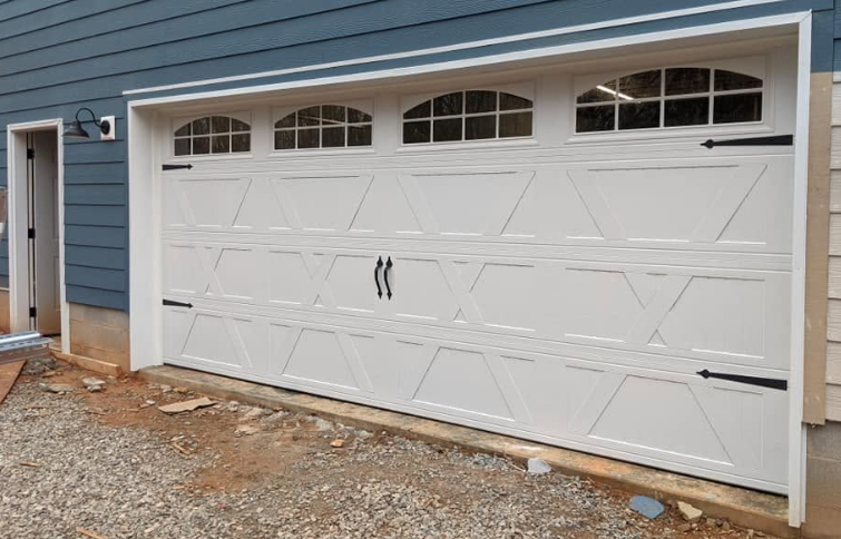 White double garage door with decorative windows on a blue house exterior, beside a gravel driveway
