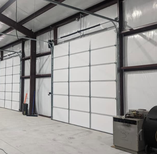 Interior of a large empty warehouse with white roll-up doors, steel beams, and a concrete floor