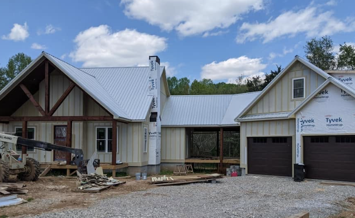 Partially built house with white siding, metal roof, and garage under construction on a gravel lot