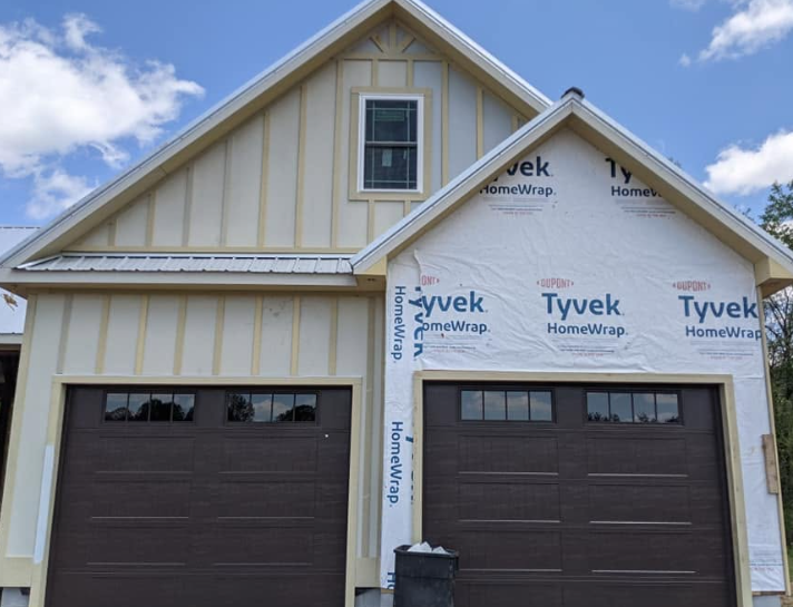 Front view of a new house exterior with two garage doors and Tyvek house wrap on the upper right wall