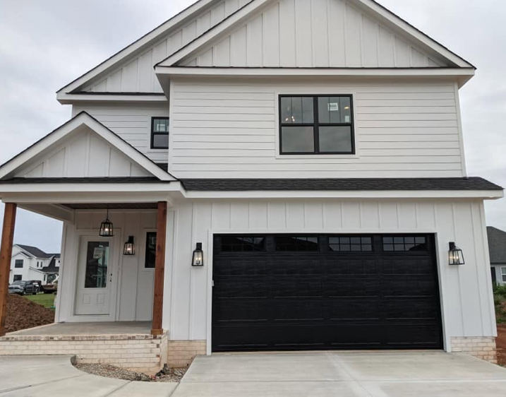 Modern two-story white house with black garage door and covered front porch