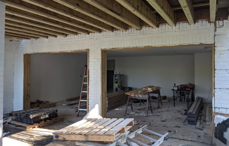 Partially renovated room with exposed ceiling beams, white brick walls, ladders, and construction materials on the floor