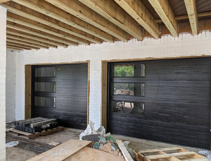 Construction site interior with two black garage doors under exposed wooden ceiling beams