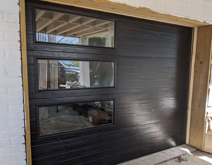 Black garage door with three narrow windows in a residential entryway under construction