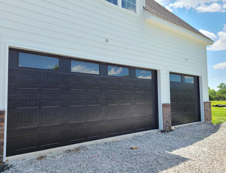 Black garage door and side entry door on a white house with gravel driveway.