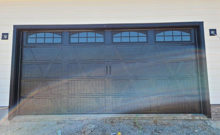 Black double garage door with four arched windows, set in a light exterior wall.