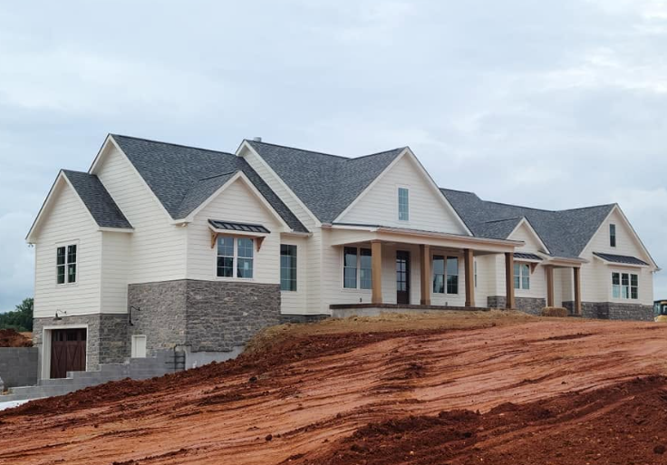 Newly built beige house with stone accents and a front porch on a red dirt lot