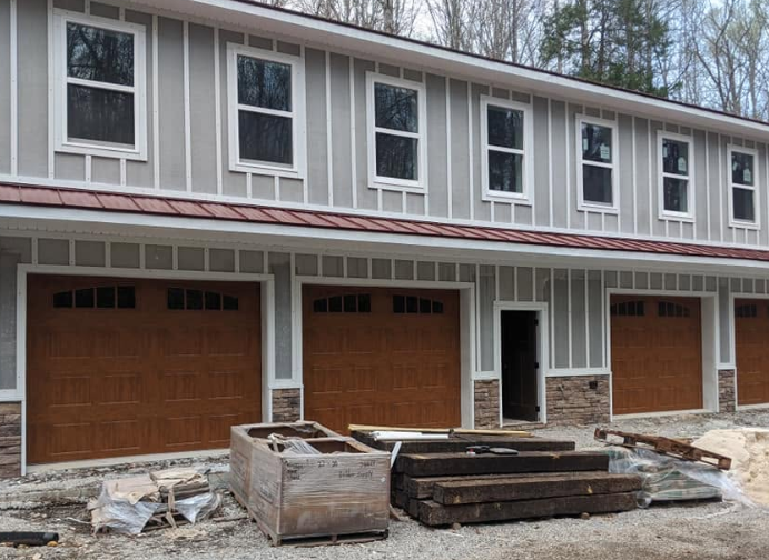 Row of unfinished townhouses with brown garage doors and construction materials in front