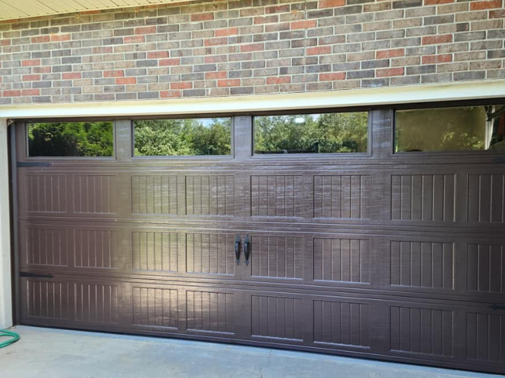 Dark brown garage door with small windows beneath a brick wall.