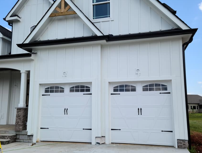 White double garage doors on a house exterior with black trim and dormer windows