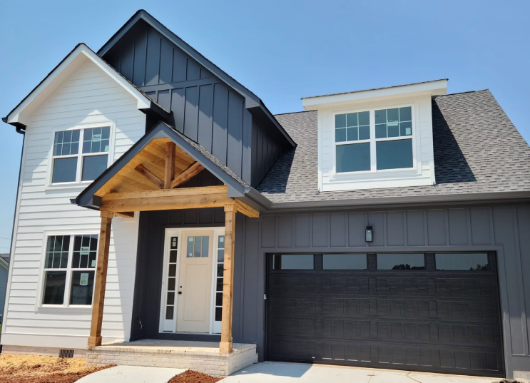 Modern two-story house with gray siding, black garage door, and covered front porch under a blue sky