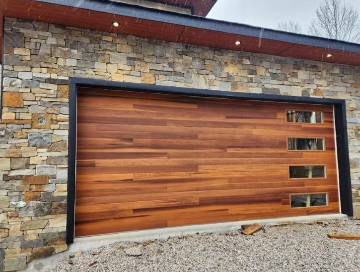 Modern wooden garage door with black trim set into a stone wall.