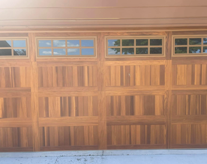Wooden garage door with four small windows along the top, viewed in bright sunlight.