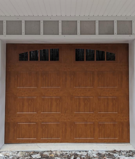 Wooden garage door with small upper windows beneath a white overhang.