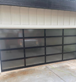 Black-framed frosted glass garage door beneath white siding on a concrete driveway
