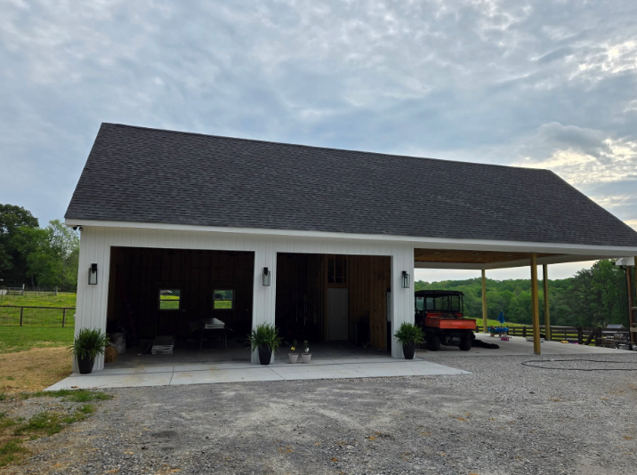 White barn-style garage with open bays and a red utility vehicle on a gravel driveway under a cloudy sky