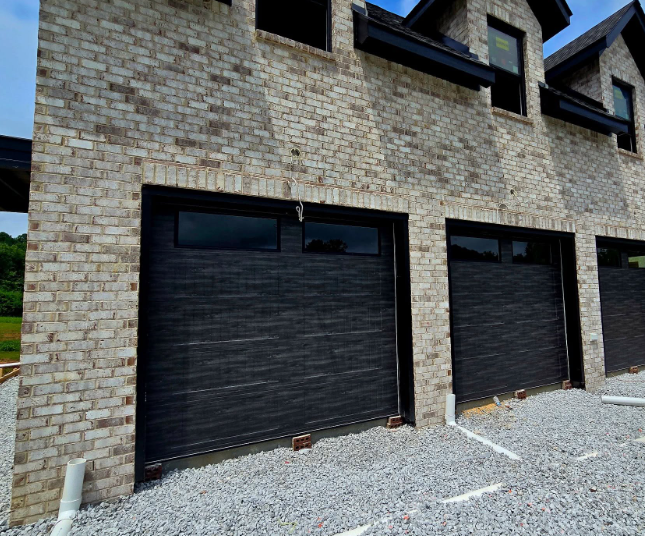 Stone townhouse exterior with three black garage doors and gravel driveway