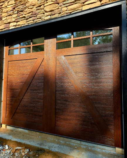 Wooden garage door with small upper windows set in a stone wall, lit by sunlight