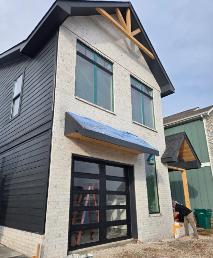 Modern two-story house with dark siding, light stone facade, and blue awning over the front entry.