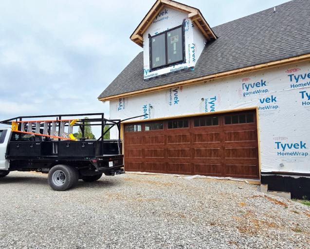 Truck parked by a house under construction with Tyvek wrap and a wooden garage door in front.