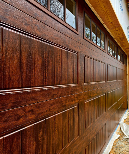 Close-up of a reddish-brown wooden garage door with decorative panels and windows at the top