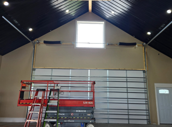 Interior of a church hall with a large cross-shaped window, metal wall panels, and a red ladder lift