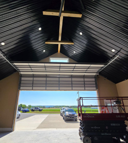 Inside a hangar with open garage door, looking out to a runway and parked vehicle in daylight
