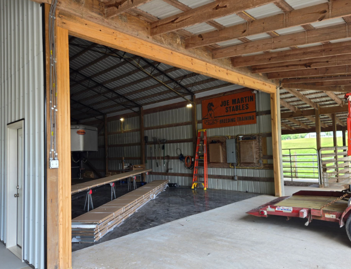 Interior of a partially built barn with exposed framing, ladder, and stacked boards on the floor