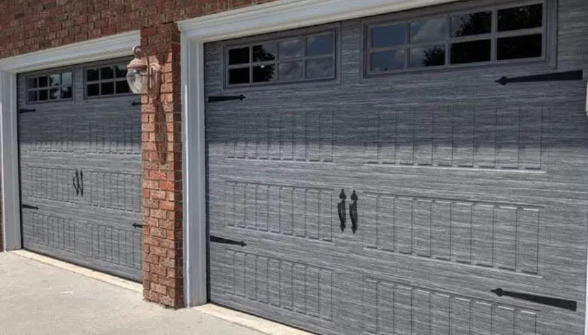 Two gray garage doors with decorative windows and brick pillars on a driveway