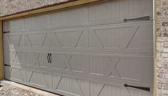 Closed beige garage door with decorative geometric panels and black handles, set in a stone wall