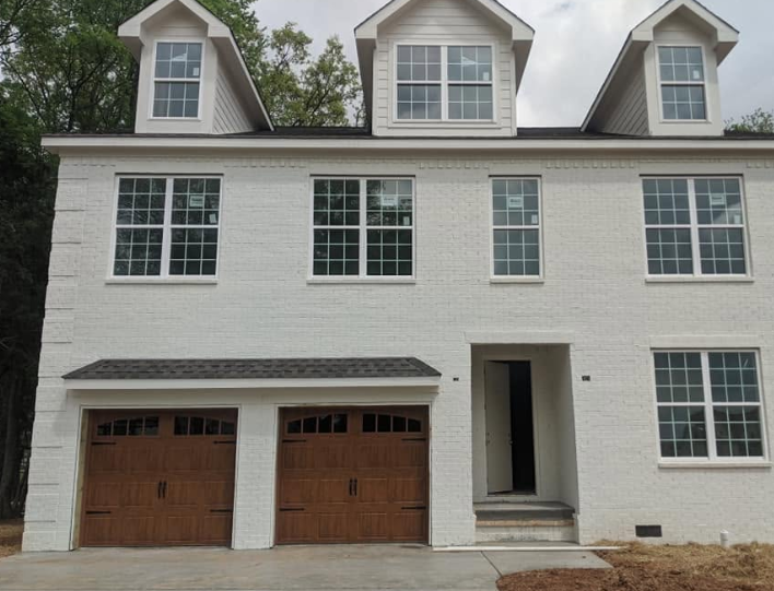 White three-story house with two wooden garage doors, large windows, and a front entry porch