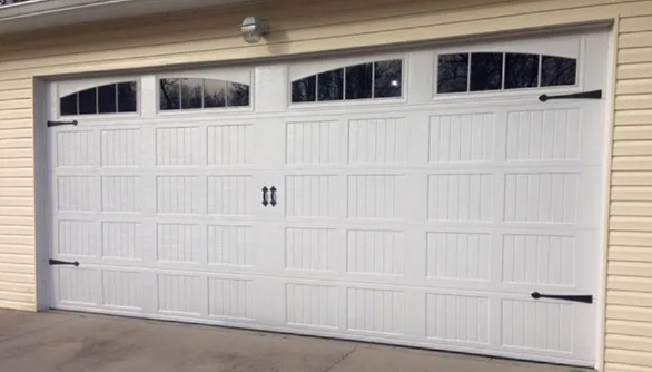 White double garage door with four window panels, set in a beige house exterior.