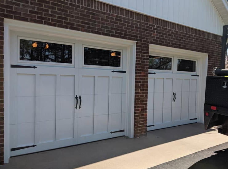 Two white carriage-style garage doors on a brick house exterior