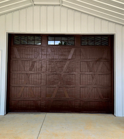 Brown garage door in a white metal building with a concrete driveway and small upper windows