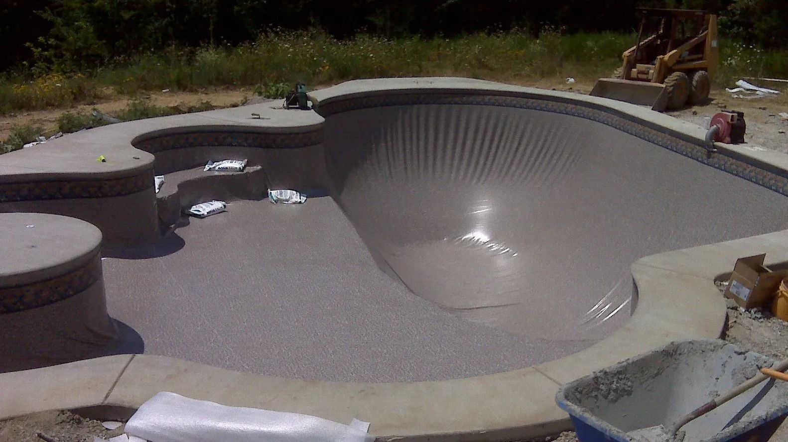 Newly constructed, empty swimming pool bowl with textured gray plaster finish.