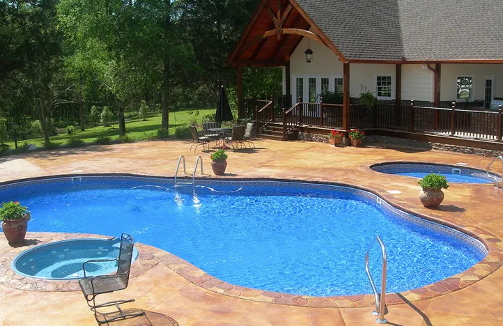 Pool with blue water and two hot tubs on a concrete patio in front of a house.
