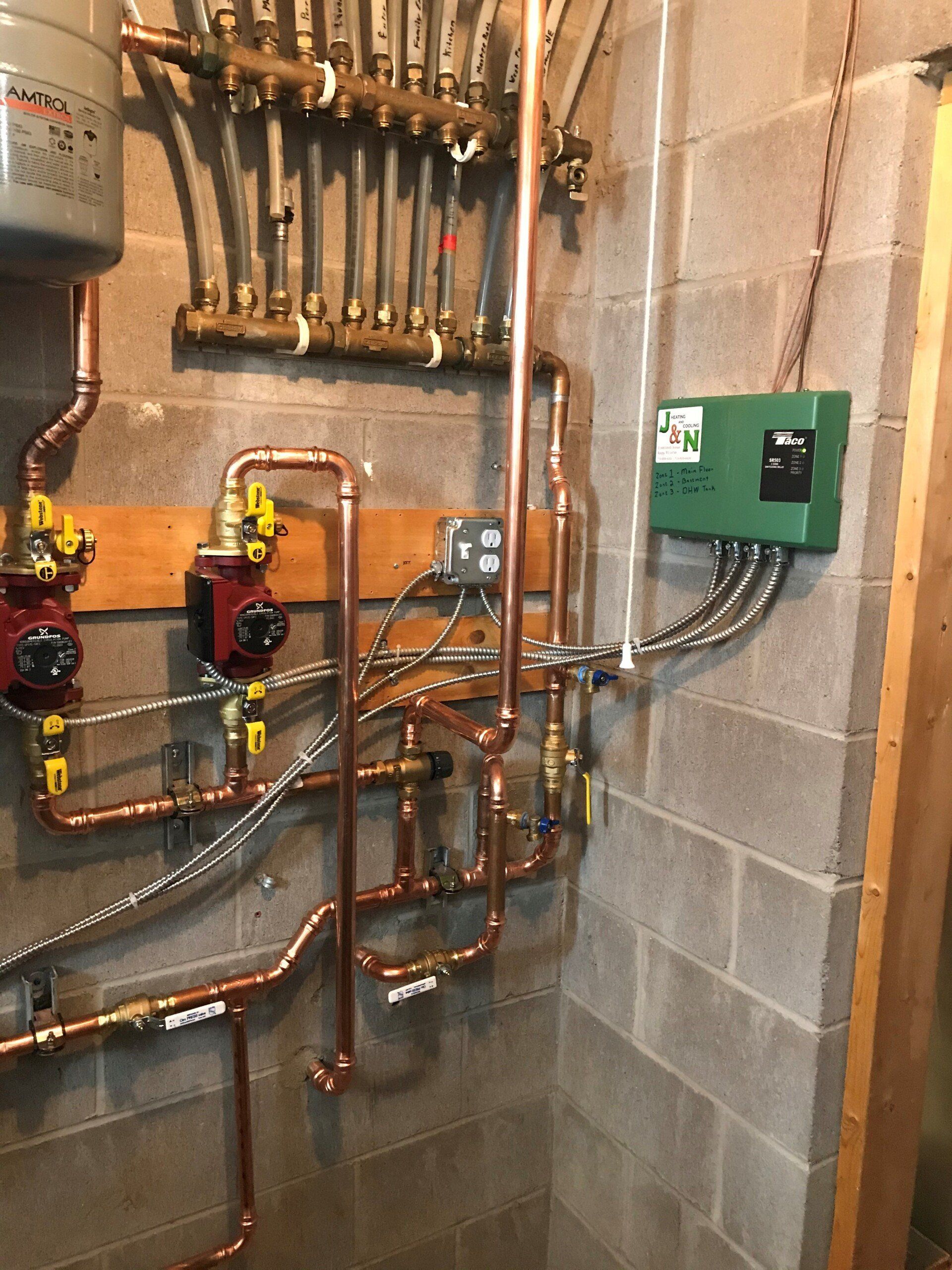 Copper pipes and fittings in a utility room, with pumps, a green control box, and a hydronic heating manifold.