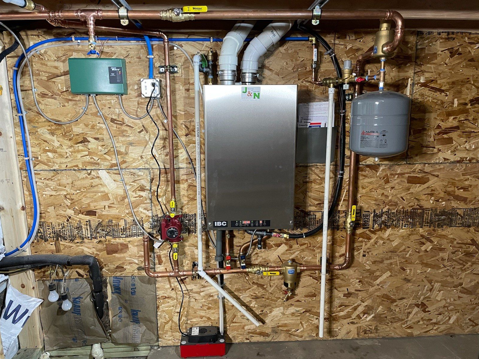 A wall-mounted heating system with copper piping and a red pump, installed on a wood-paneled wall.