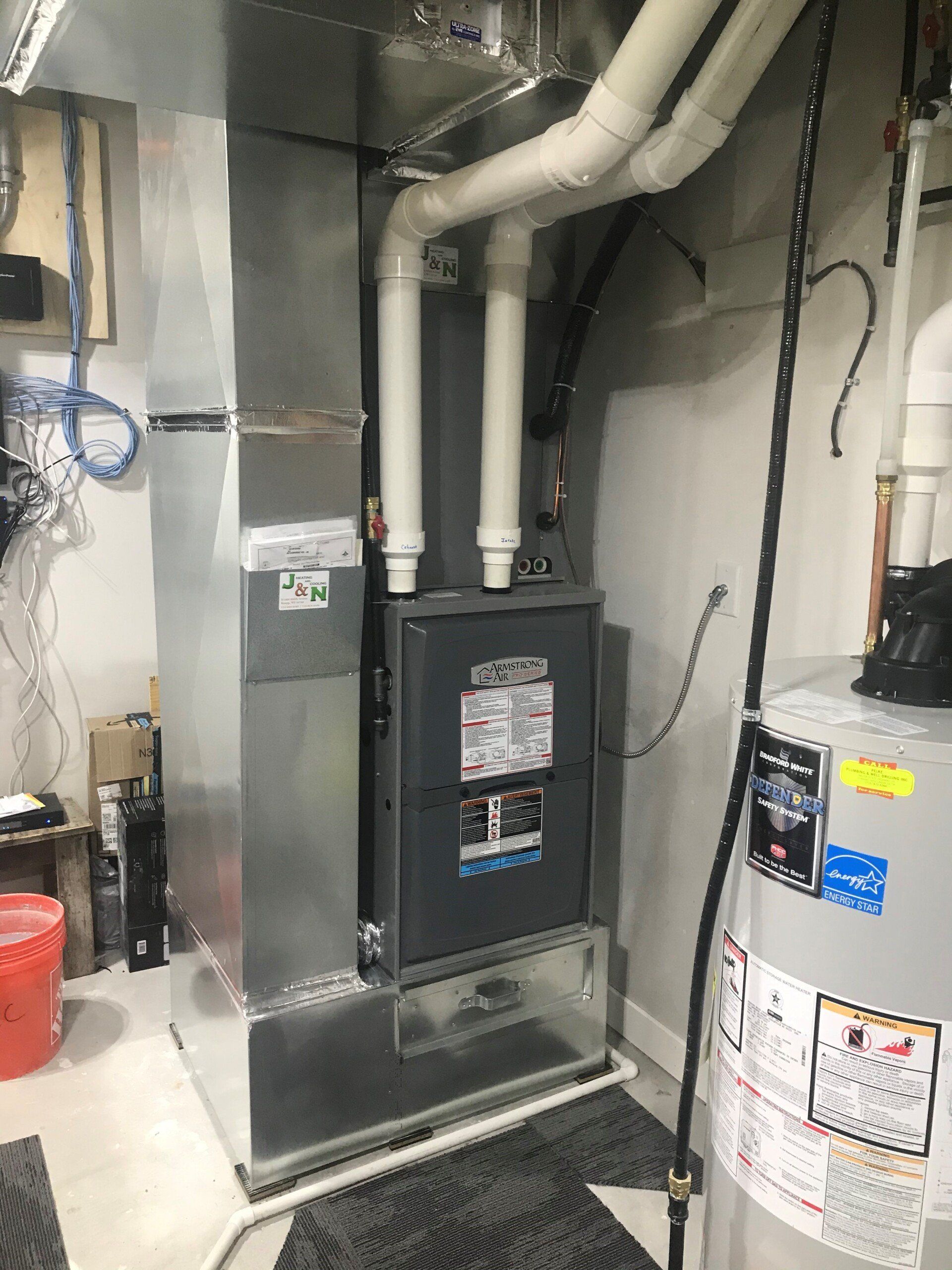 A furnace and hot water heater in a basement setting. The silver furnace has ductwork attached and sits next to the hot water heater.