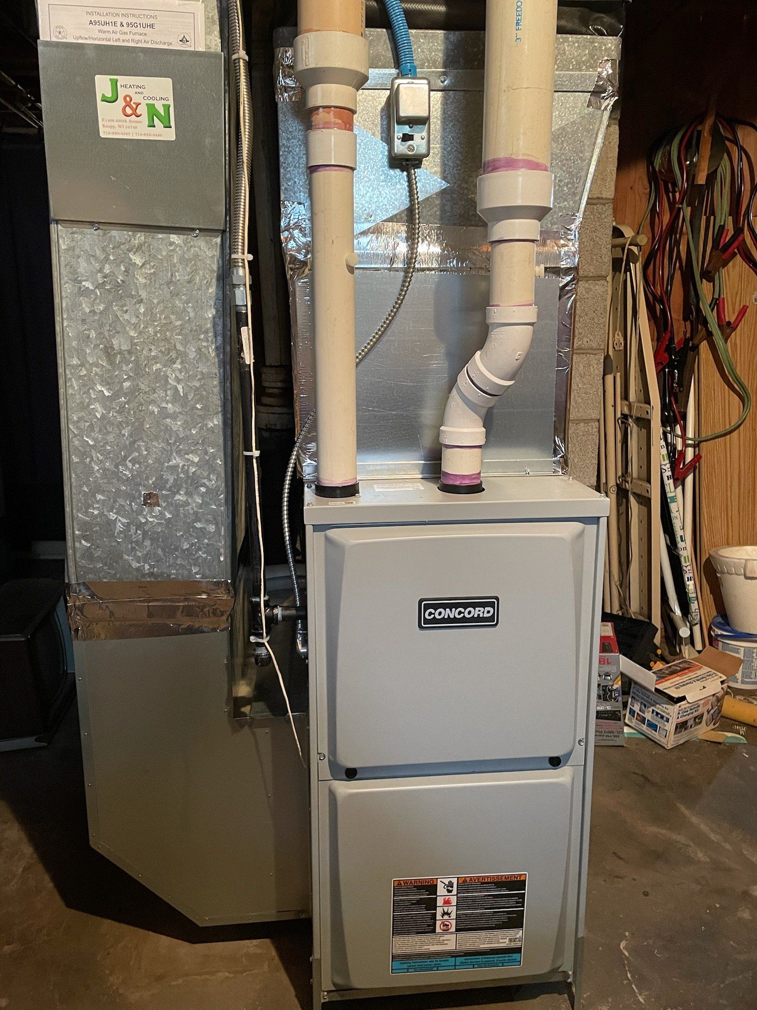 A gas furnace in a basement. The gray furnace is flanked by ductwork and PVC pipes.