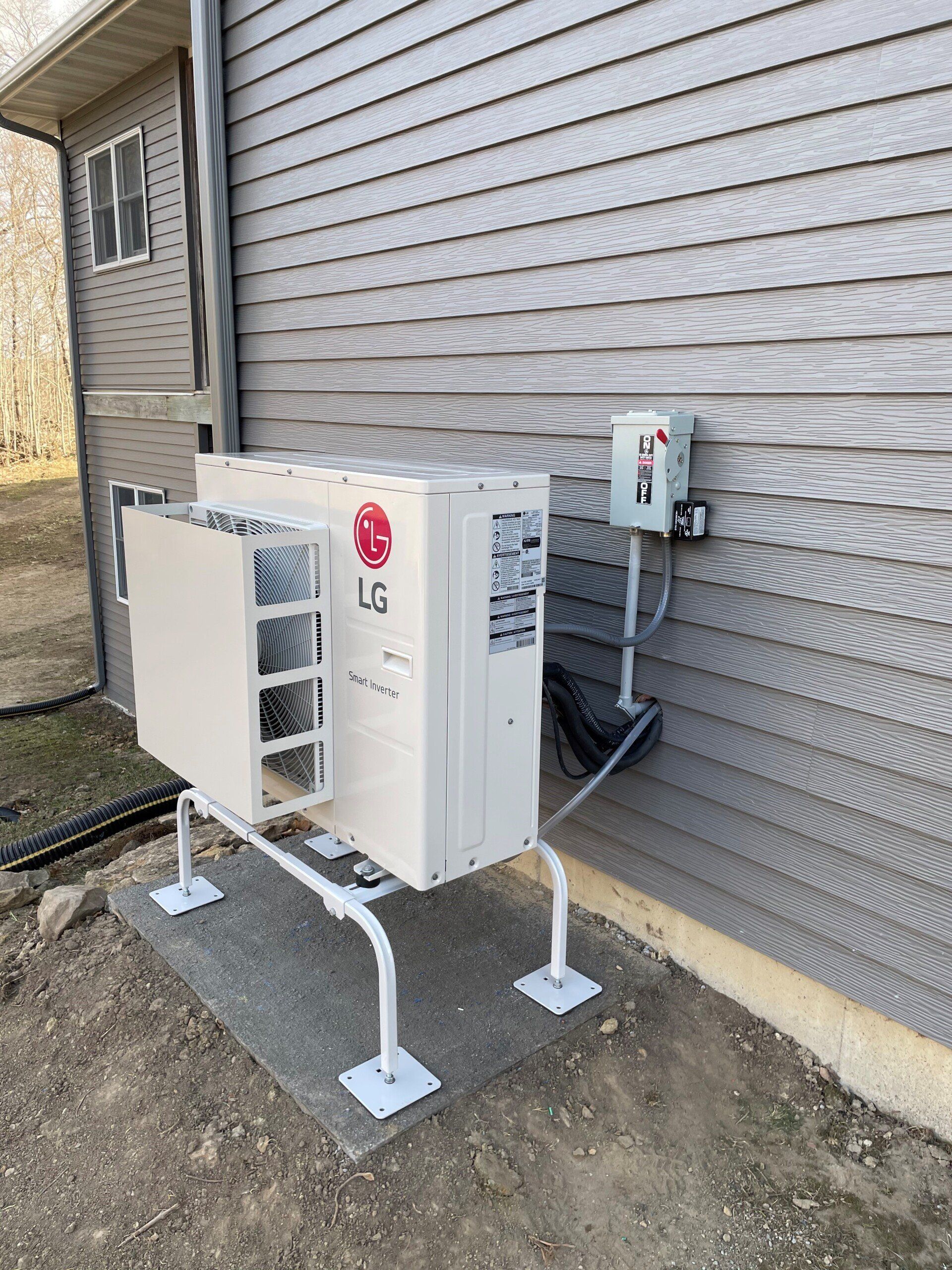 LG outdoor HVAC unit mounted on a stand next to a house with gray siding. A gray concrete pad sits beneath the unit.