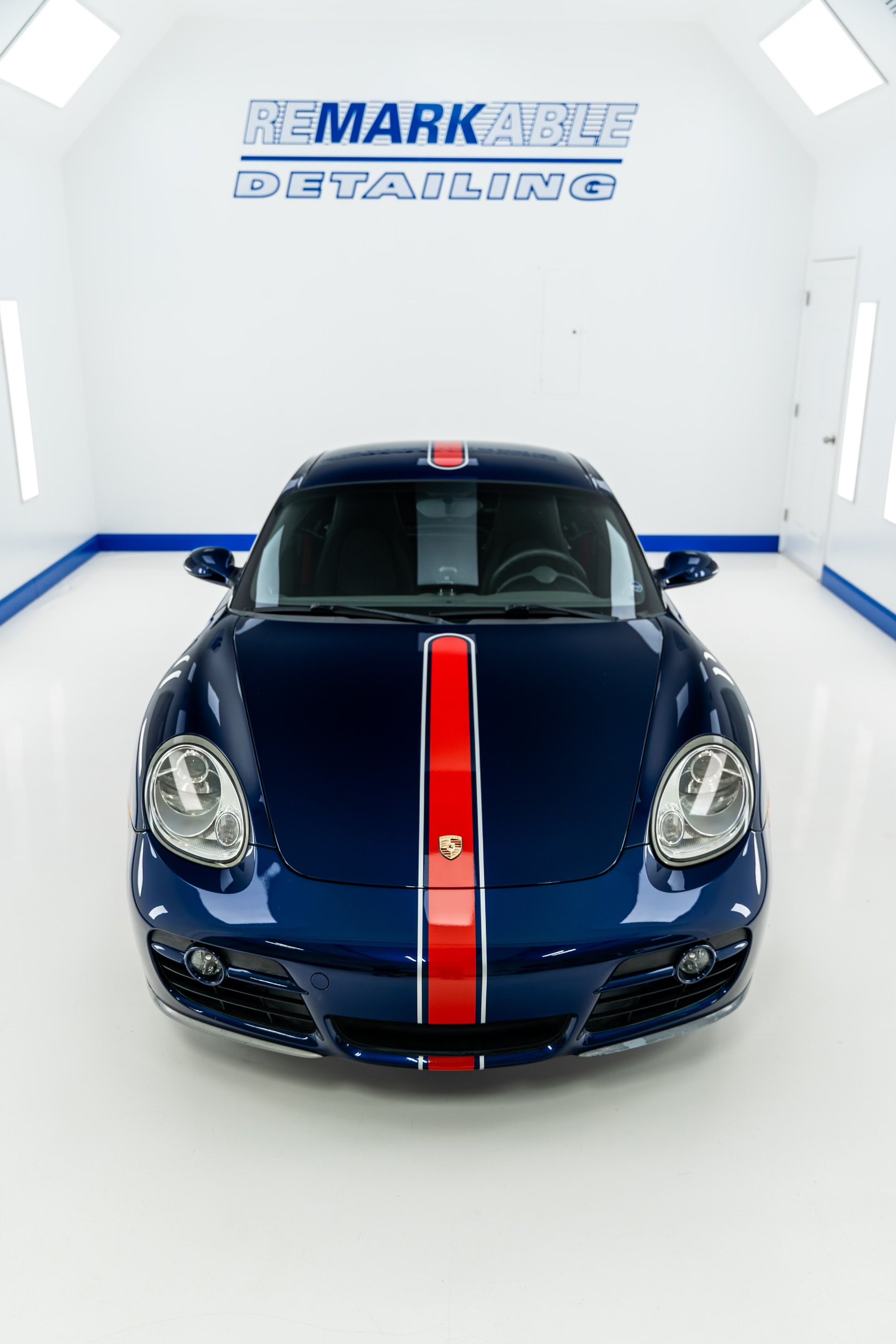 A blue car with a red and white stripe on the hood is parked in a garage.