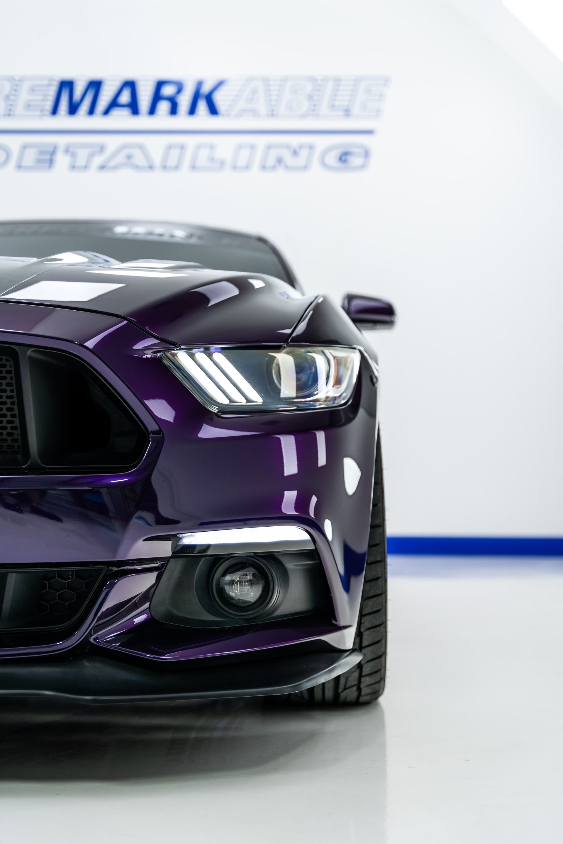 A purple mustang is parked in front of a white wall.