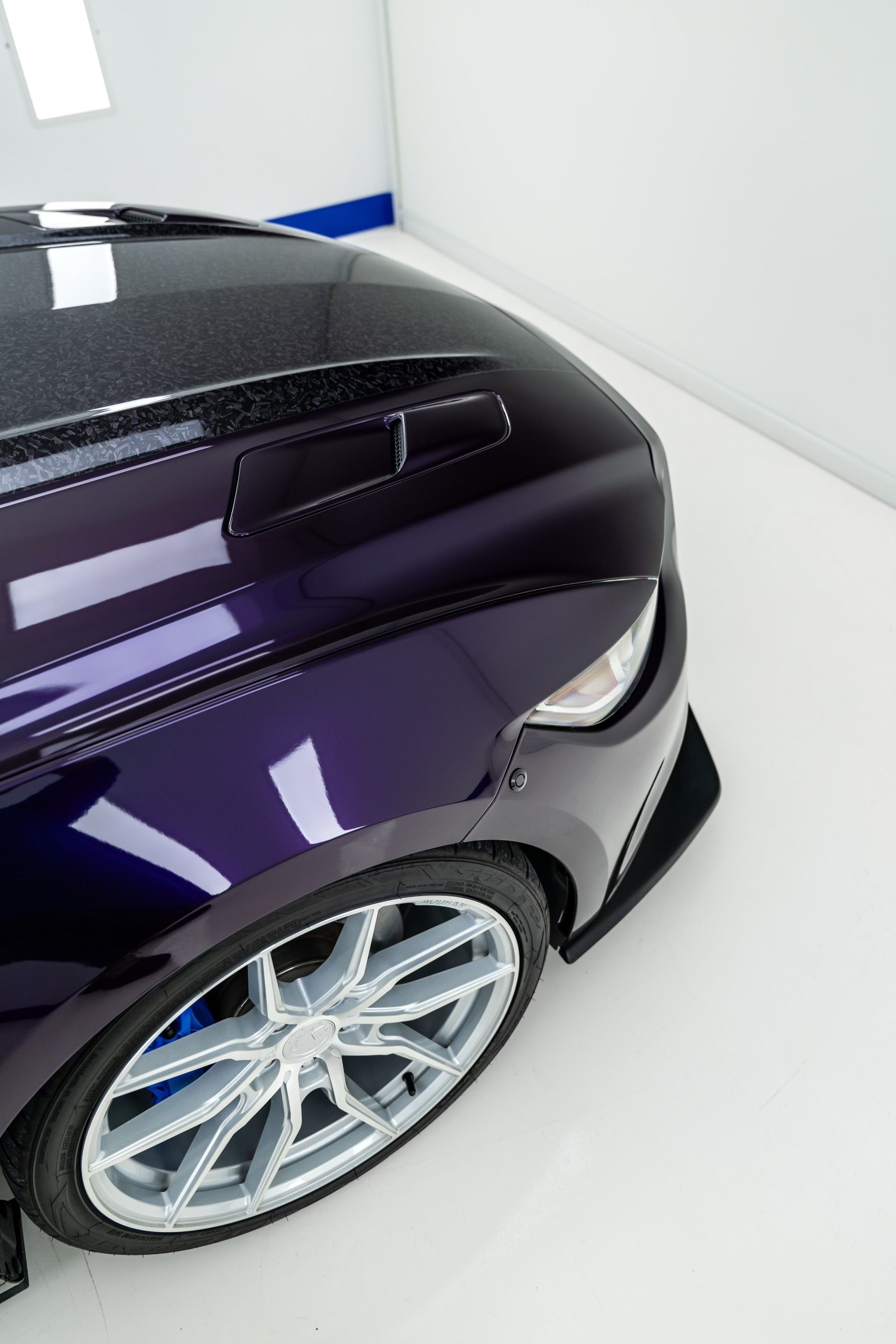 A purple car is parked on a white floor in a garage.
