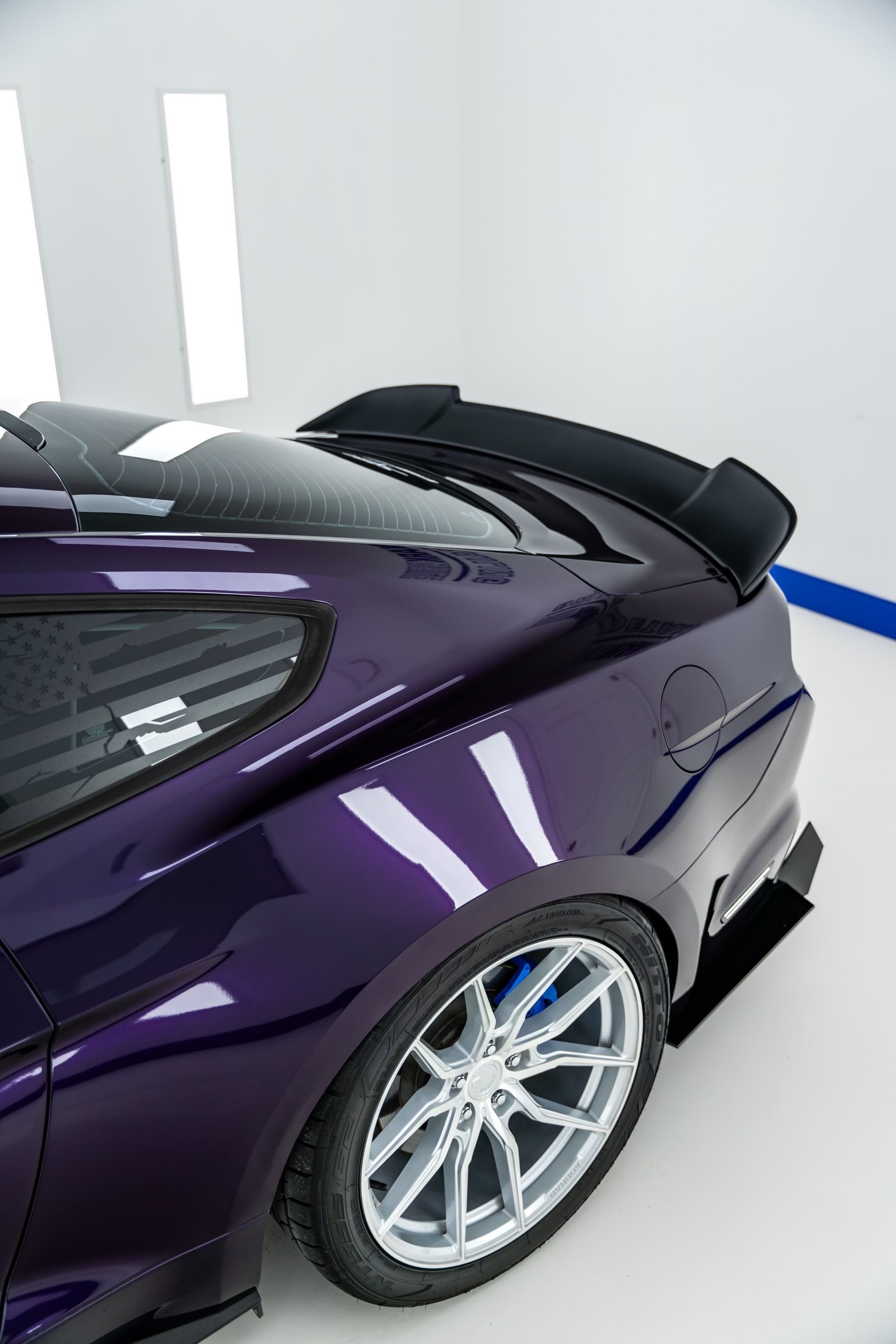 A purple car with a black spoiler is parked in a garage.