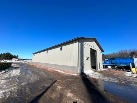 A long, light-colored industrial building with a large open doorway on a sunny day.
