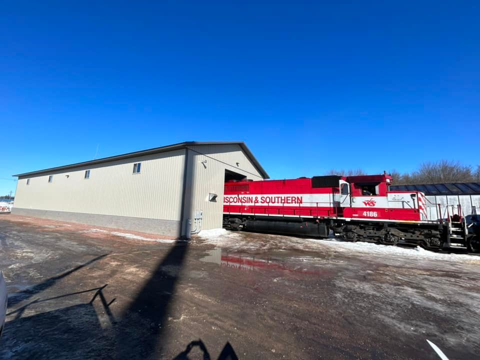 Red metal barn with a porch and open garage door, under a clear blue sky.