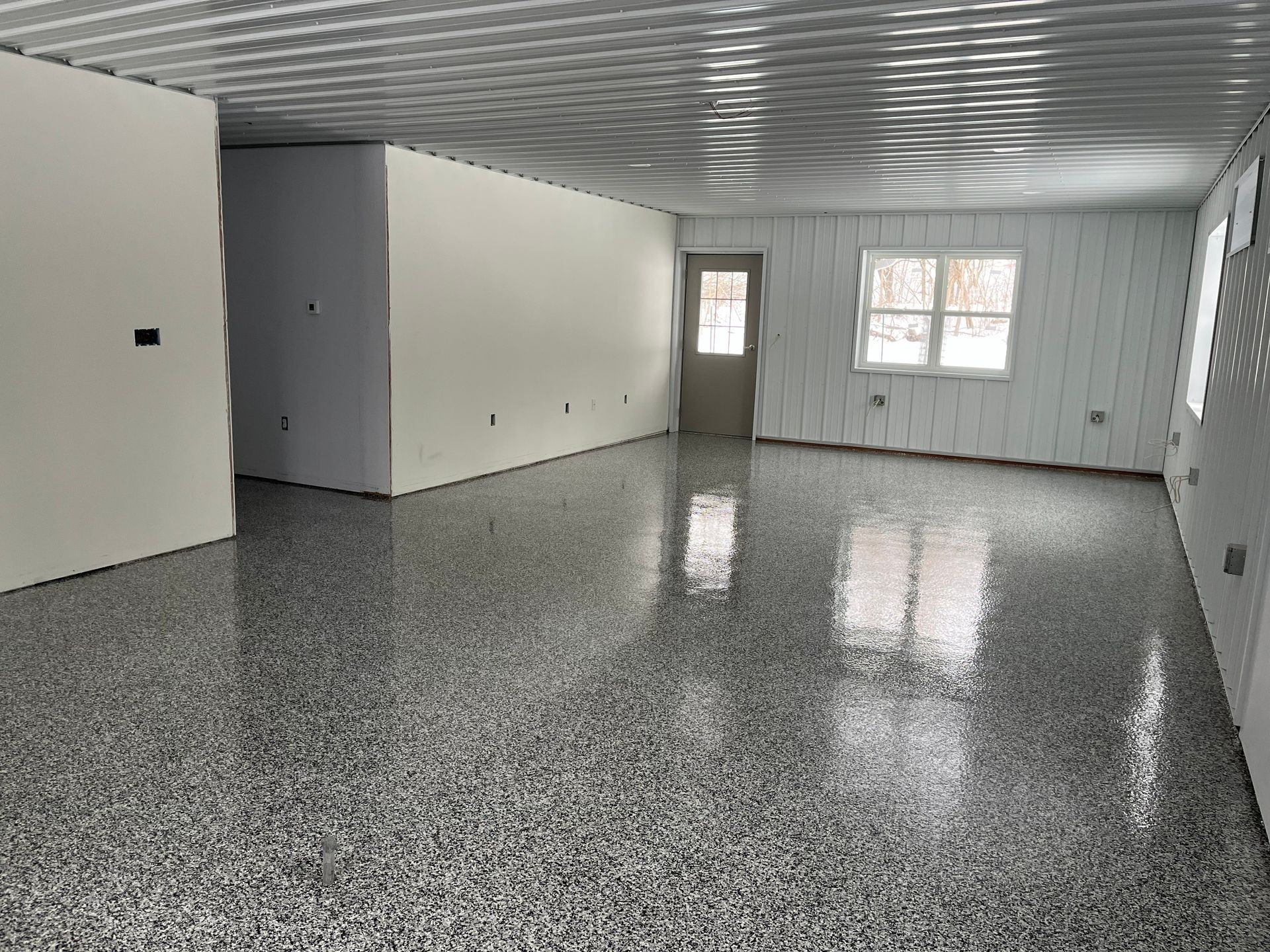 Spacious interior with gray epoxy floor, white walls, and a door to the outside.