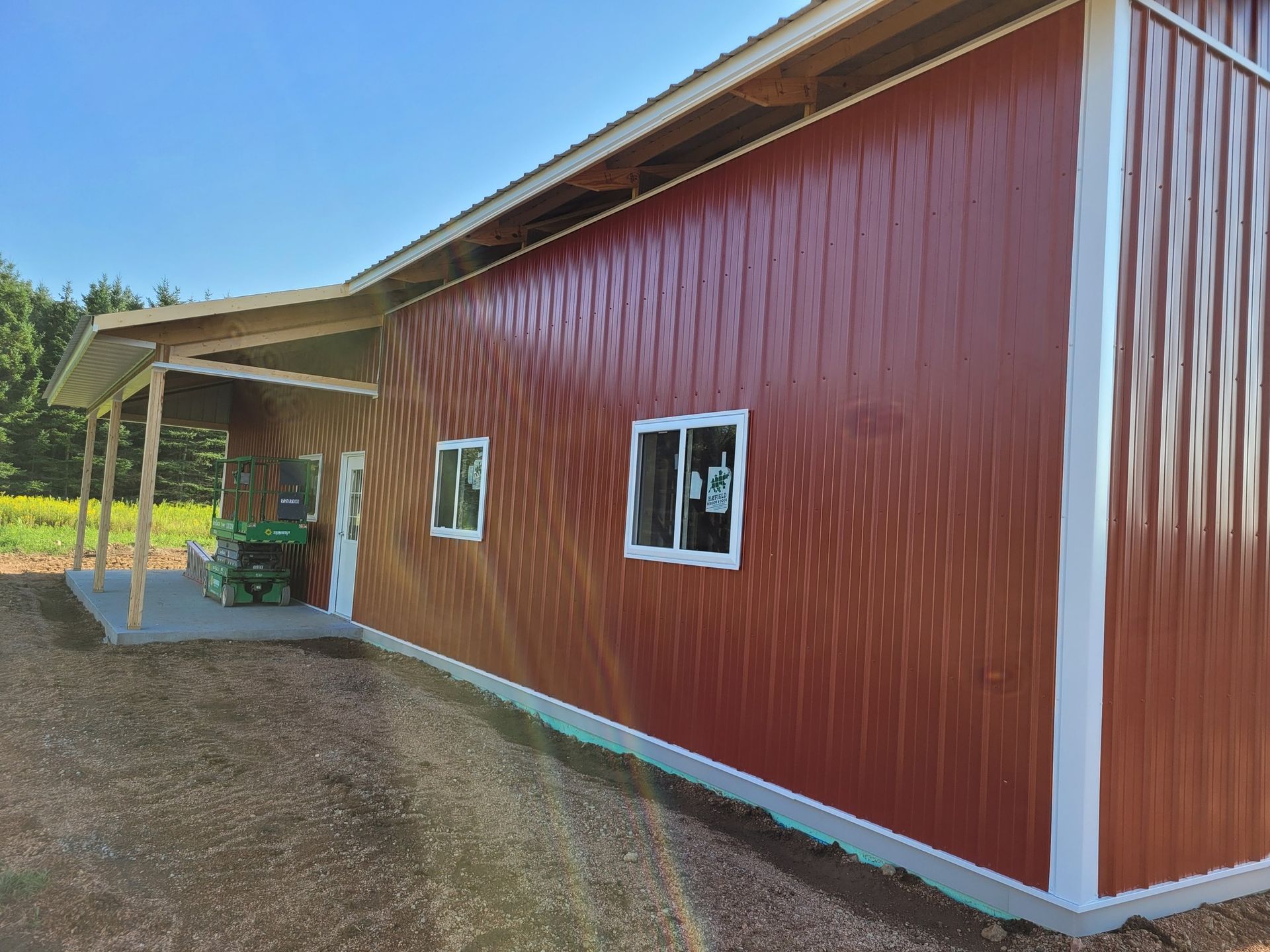 Red metal-sided building with white trim, a porch, and two windows. A tractor sits on the porch.