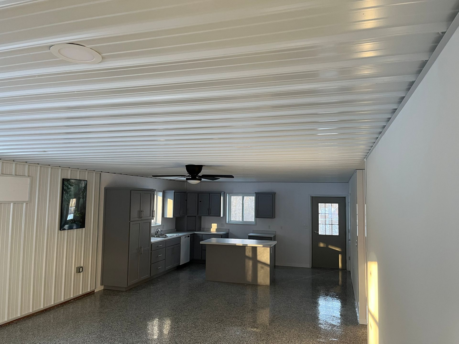 Interior of a modern kitchen with gray cabinets, island, and concrete floors; corrugated metal ceiling.